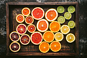 Citrus fruits (orange, blood orange, grapefruit, lemon, lime) halved and sorted by colour in a rustic wooden crate with fresh citrus leaves