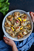 Woman holding a round baking tin filled with fried artichokes