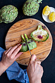 Women's hands cutting an artichoke on a wooden board