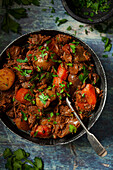 Beef stew in a metal bowl with carrot and potato and garnished with chopped parsley.