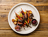Grilled venison steak with baked vegetables and berry sauce on a wooden base