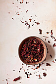 Dried hibiscus flowersin a bowl on a pink worktop.