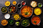 Indisches Essen Curry-Butterhähnchen, Palak Paneer, Chiken Tikka, Biryani, Gemüsecurry, Papad, Dal, Palak Sabji, Jira Alu, Reis mit Safran auf dunklem Hintergrund