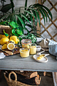 Hausgemachter Lemon Curd in Gläsern, umgeben von Zitronen in einer rustikalen Küche