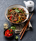 Stir fry noodles soba with beef and vegetables in bowl on dark stone background