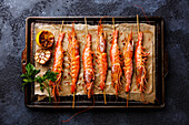 Grilled fried prawns Langostino Austral on skewers on metal grid baking tray on black background