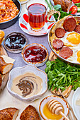Tahin Pekmez in einer Schale und andere türkische Frühstücksspeisen wie Marmeladen, Eier und Sujuk, Menemen und türkischer Tee dahinter
