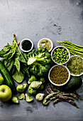 Healthy Green food Clean eating selection Proteinquelle für Vegetarier: Spargel, Apfel, Avocado, Brokkoli, Spinat, Spirulina, grüne Erbsen auf grauem Betonhintergrund copy space