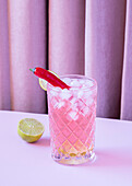 Klares Glas gefüllt mit erfrischendem kalten Cocktail mit Pfeffer und Eiswürfeln auf dem Tisch mit Limette serviert