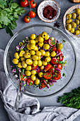 Gehackte Zwiebeln, grüne Zwiebeln, Petersilie, Dill, halbierte Kirschtomaten und entsteinte grüne Oliven in einer Glasschale