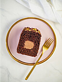 Travel Cake oder Tube Cake oder Voyage Cake, gefüllt mit Ganache in der Mitte und gekrönt mit Schokoladenglasur und Pistazien (kann auch mit Erdnüssen gemacht werden). Schokoladenkuchen mit Schokoladen-Sahne-Käse-Füllung in der Mitte. Idee und Rezept zum Backen mit Ganache-Creme-Einsatz. Laibkuchen auf Frauenhänden