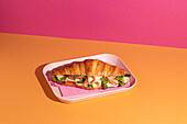 Leckeres Croissant mit Schinken, Käse und Rucola auf einem Teller mit buntem Hintergrund von oben