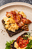Scrambled eggs with bacon and tomato on toasted grain bread