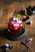 Bramble cocktail with violet flower, mint and lavender on a wood backdrop
