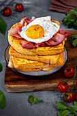 A stack of eggy bread slices topped with fried bacon and egg.