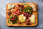 Italienische Snacks mit Schinken, Oliven, Käse, sonnengetrockneten Tomaten, Wurst und Brot auf einem hölzernen Schneidebrett vor einem konkreten Hintergrund