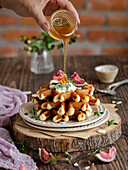 Waffelstapel mit Feigen, Sahne und Thymian mit flüssigem Honig, auf einem rustikalen Holzbrett