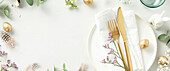 Easter table decoration. Stylish Easter brunch table decoration with white plate, napkin, golden cutlery, Easter eggs and spring branches on a light grey background in top view copy space