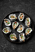 Frisch geschälte Austern mit Buttermilchdressing, Lachsrogen, Balsamico-Perlen und Kräuteröl auf Steinsalz auf einem schwarzen Teller