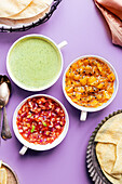 Three poppadom dips: mint yoghurt sauce, red onion chutney, mango chutney, served with poppadoms