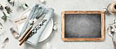 Banner. Table setting. A fashionable minimalist plate with a linen napkin, knife, fork, chalkboard, Easter eggs and feathers on a grey background. View from above. Happy Easter concept for cafes and restaurants. Copy space