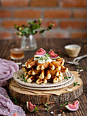 Pile of waffles with figs, cream, thyme and honey on a rustic wooden board