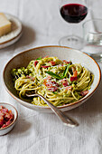 Angled shot of a bowl of spaghetti with fresh basil, pancetta, parmesan and a glass of red wine