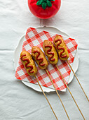 Corn dogs, simply presented on white plate with chequered napkin and tomato sauce