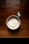 Bowl of yoghurt on an antique wooden table with silver spoon