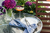 Vase with purple hydrangeas places on table near glass with drink and ceramic plate in garden