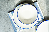 Top view of minimalistic rustic table setting with white plates and striped napkin on gray surface in daylight