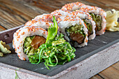 Nahaufnahme einer servierten Reihe von Avocado-Thunfisch-Uramaki-Sushi-Rollen mit Wakame-Salat auf einem Betonteller