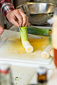 High angle close-up of an anonymous chef trimming fresh leeks on white cutting board in kitchen