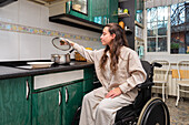 A woman in a wheelchair comfortably reaches for a pot lid while cooking in an adapted kitchen space