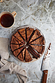 Top view of cup of hot tea placed on table near knife and chocolate cake sliced on transparent plate