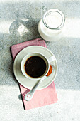 Draufsicht auf eine Tasse würzigen Espresso neben einem Löffel mit roter Paprika auf einem grauen Tisch neben einer Flasche Milch bei Tageslicht
