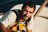 Porträt eines männlichen Fischers in Schürze, der in die Kamera schaut und lächelt, während er auf einem Schoner in Soller auf den Balearischen Inseln auf Mallorca arbeitet