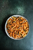 Top view of raw uncooked fusilli pasta made from wheat, beetroot and spinach in the bowl on dark green background