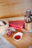 From above kitchen setup with a mortar and pestle, a checkered napkin, and saffron threads displayed on a white bowl and a glass jar, all arranged on a wooden cutting board