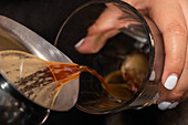 Crop anonyme Person gießt Kaffee aus der Kaffeemaschine in stilvolle Glas mit auf dem Tresen im Café