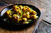 High angle of appetizing roasted cauliflower with green herbs served on black plate placed on wooden board