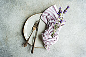 Top view of arranged flowers in napkin and fork placed on white ceramic plate with knife on gray surface