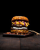Hamburger with macaroni and cheese placed on wooden tray on table against dark background
