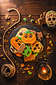 Draufsicht auf leckere Halloween-Kekse auf einem Teller, der auf einem Holztisch in der Nähe eines Seils steht