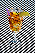 High angle of cocktail glass of Long Island ice tea made with vodka tequila light rum gin and garnished with lemon slice straw while served on stripes cloth surface