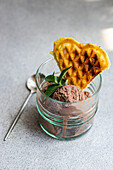 High angle of glass of homemade coffee ice cream with waffle and fresh mint near spoon on gray surface
