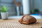 A seed-encrusted artisan bread loaf on a pine wood cutting board, with a blurred kitchen background