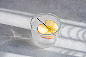 From above glass of tonic water with a slice of apple, with soft shadows and light textures in the background