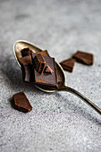 High angle of pieces of different kinds of chocolate placed on crop spoon and on gray blurred table