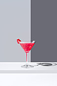 Glass filled with red pomegranate cocktails served with pomegranate seeds against a gray backdrop, casting a soft shadow